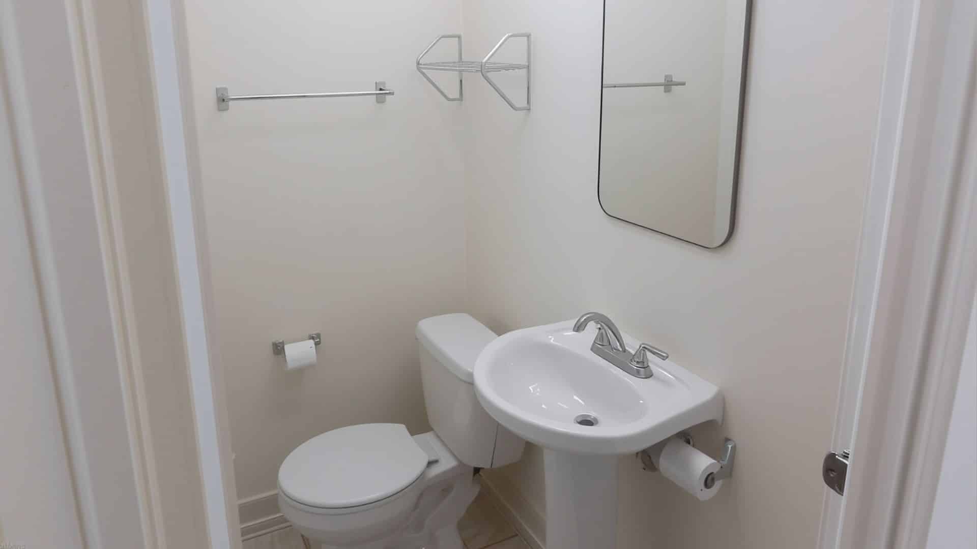 small bathroom with a white pedestal sink, compact toilet, light-colored walls, simple mirror, small wall shelf for storage, open floor area, clean and practical small bathroom design