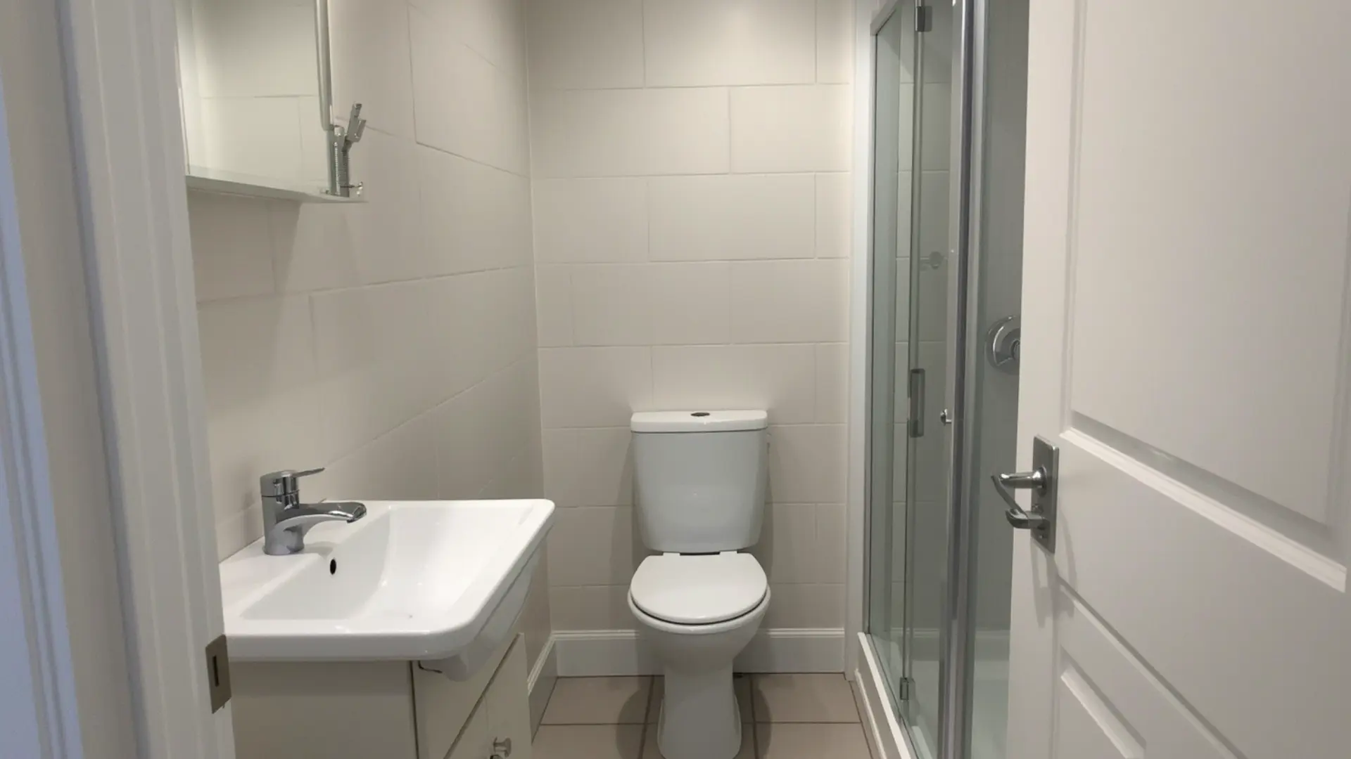 small bathroom with one-wall layout, sink, compact toilet, and shower placed along the same wall, clear walkway, light tile, slim vanity, practical space-saving design