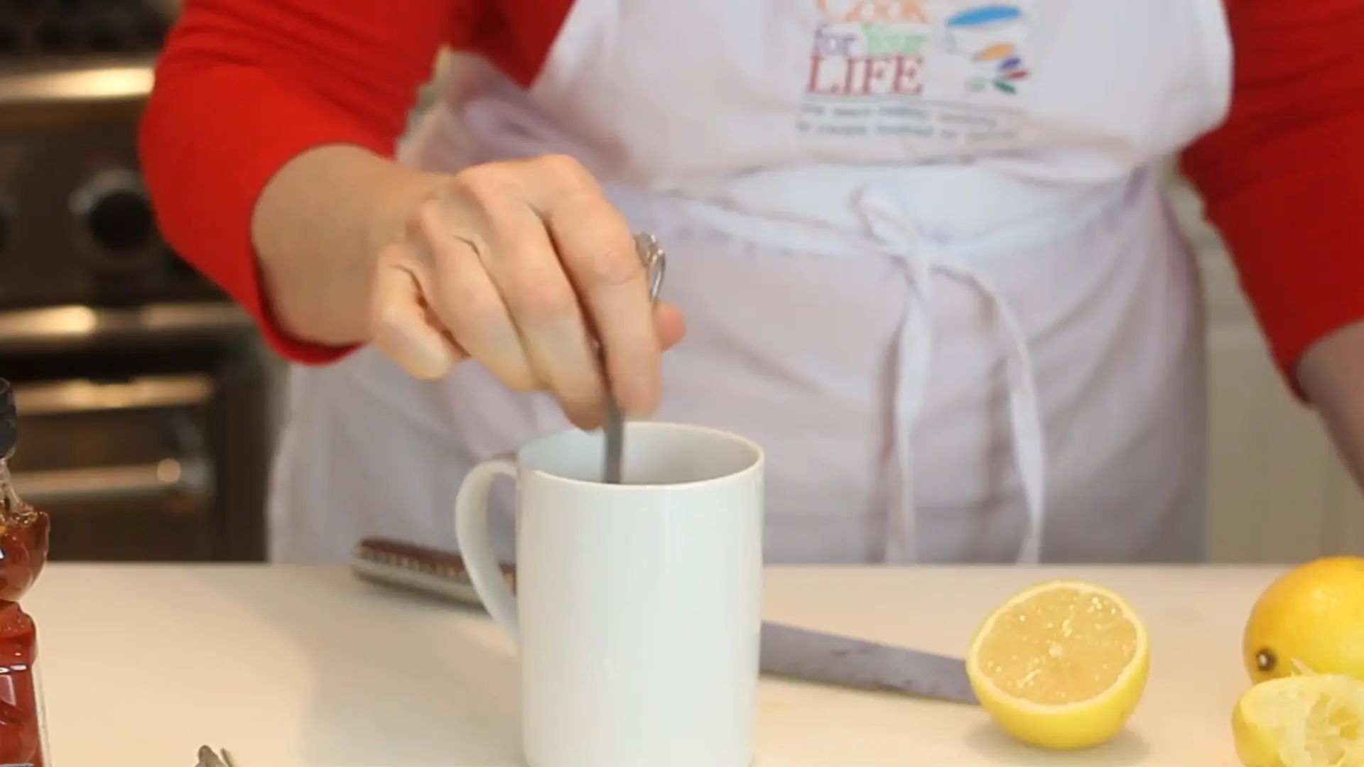 spoon stirring lemon honey drink in cup to mix ingredients evenly