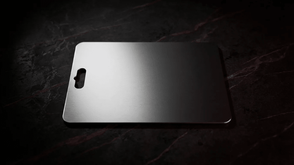 stainless steel cutting board with handle cutout on dark marble surface with dramatic lighting