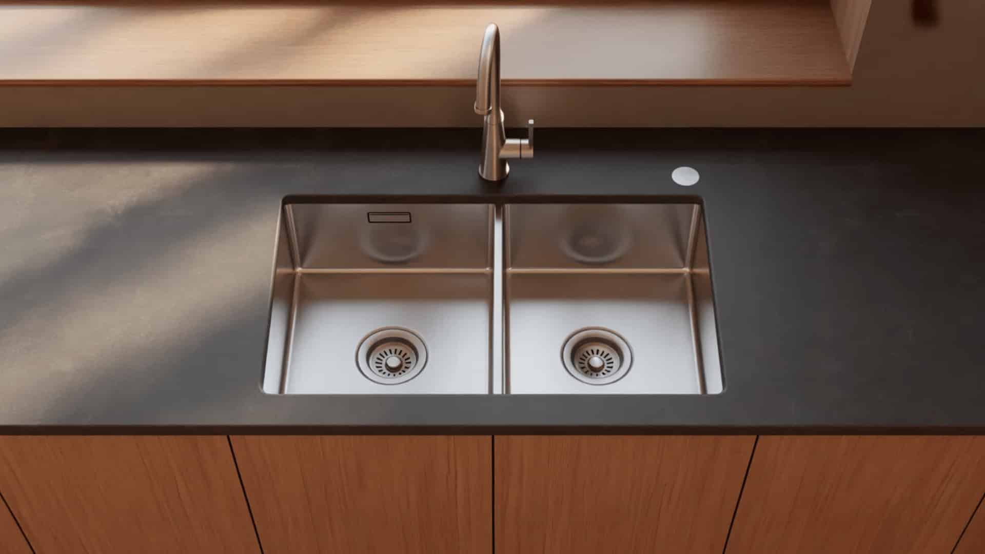 stainless steel low divider undermount sink with two unequal basins, short center wall, bronze faucet, and dark gray stone countertop