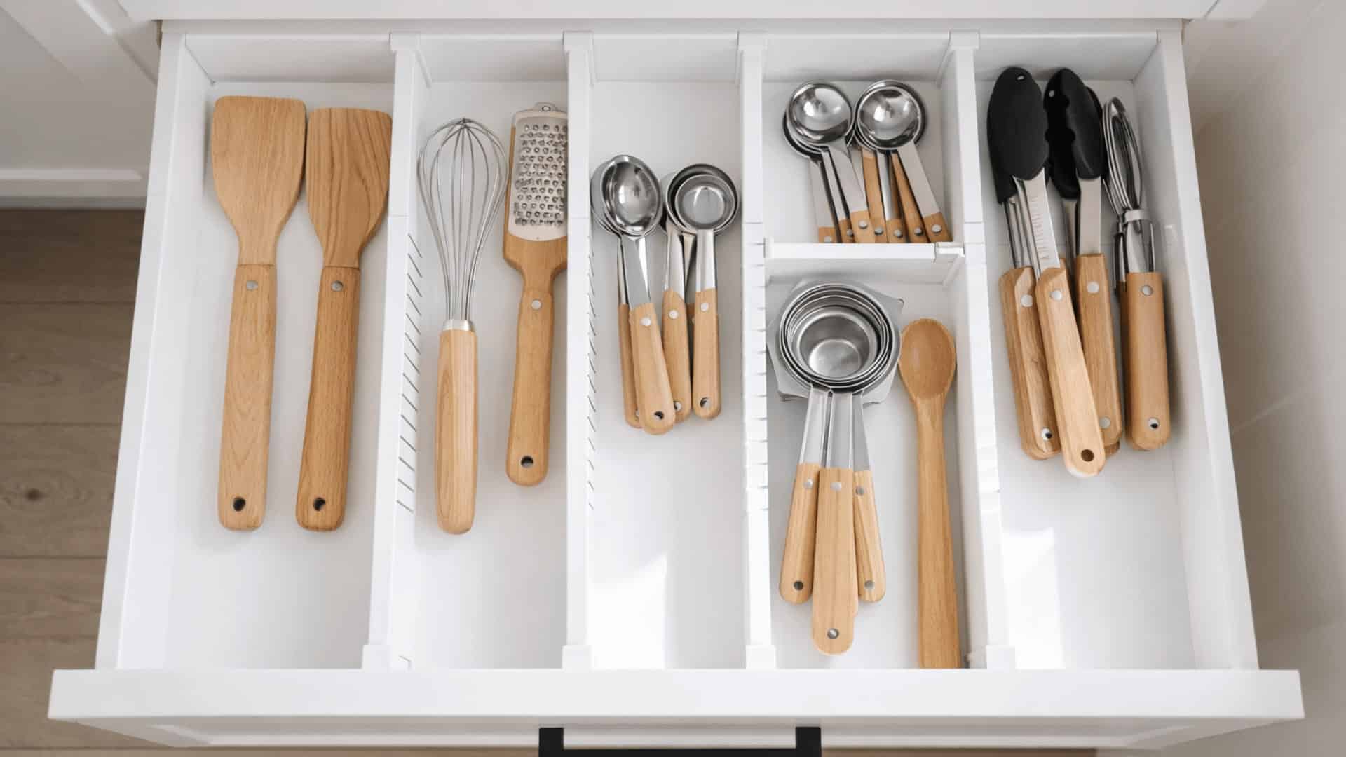 top view of an organized kitchen drawer with white adjustable dividers separating wooden handled cooking utensils