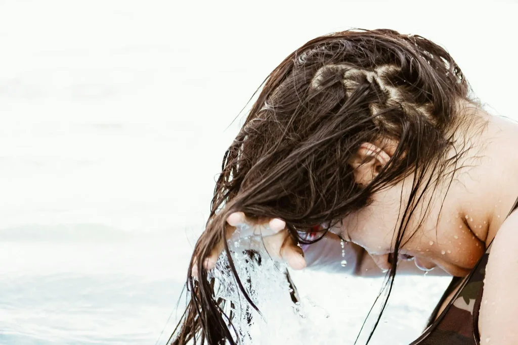 Person rinsing wet hair outdoors with water splashing