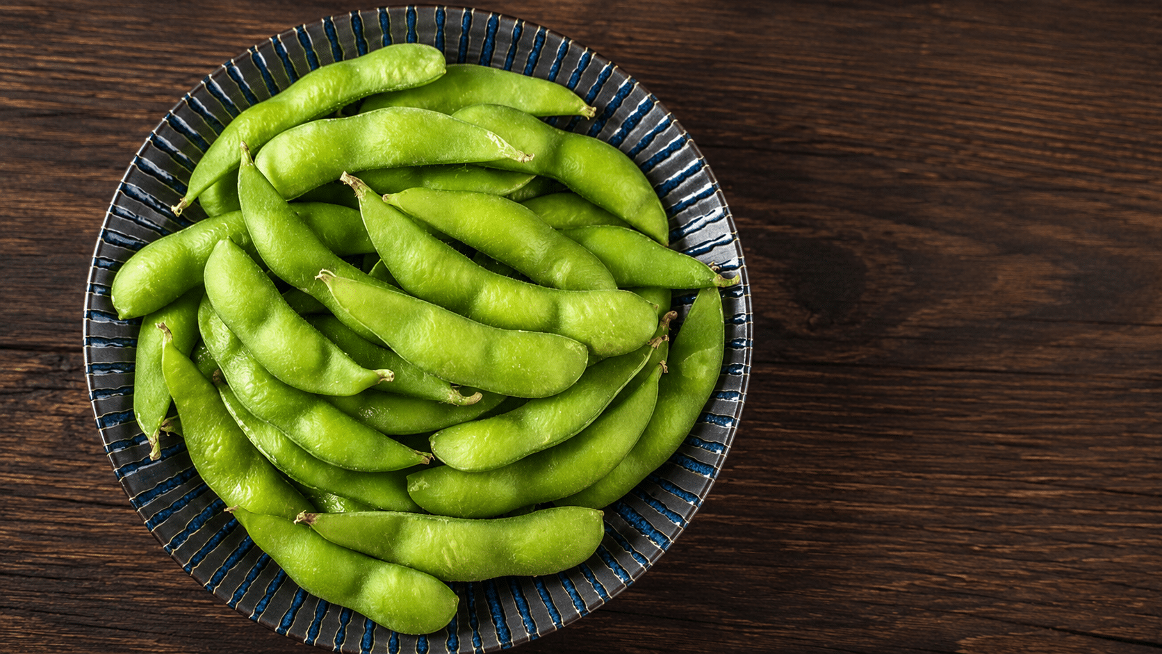 a bowl filled with fresh green edamame pods arranged on a dark wooden table creating a simple and healthy snack display