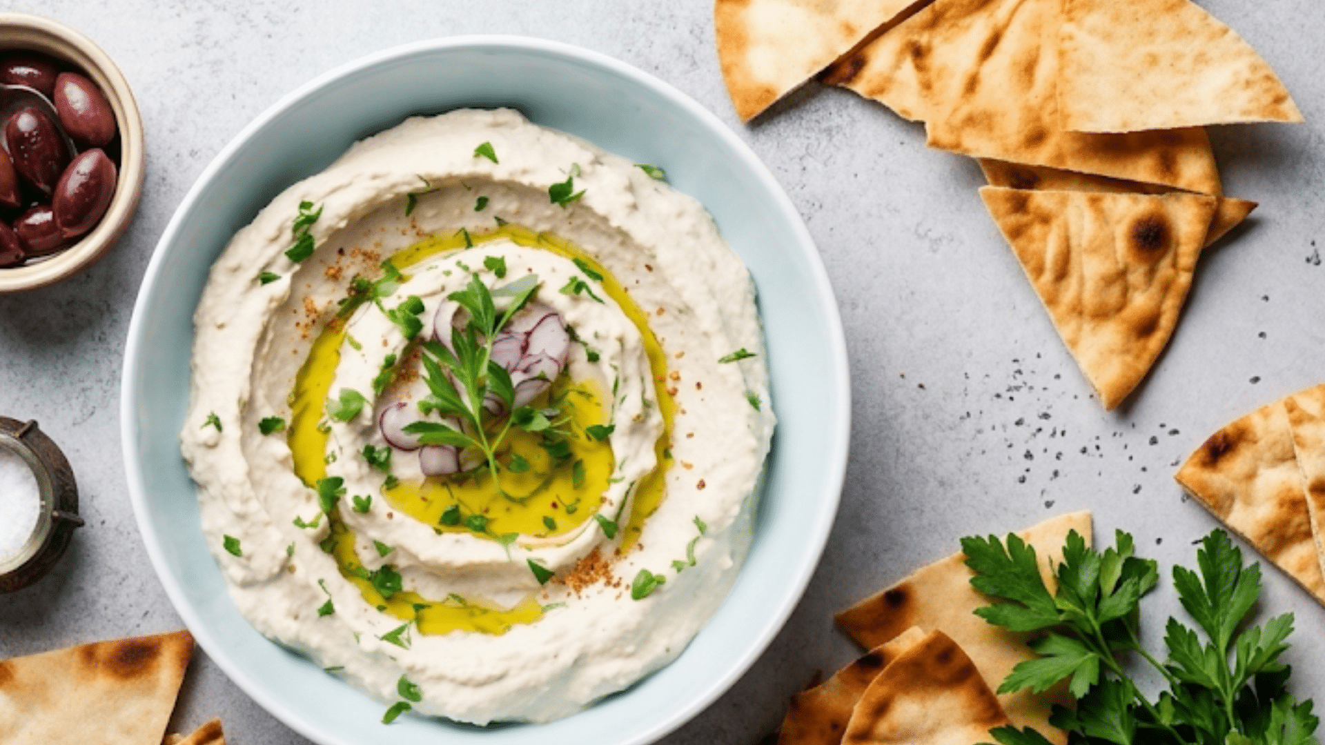a bowl of creamy hummus drizzled with olive oil served with pita bread olives and fresh parsley for a flavorful healthy snack