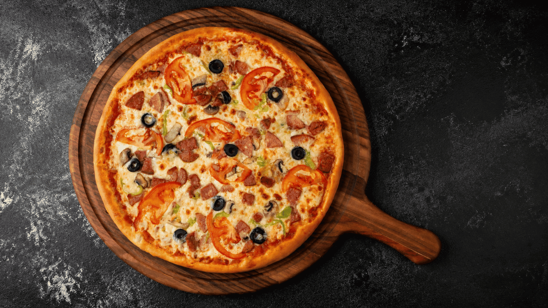 a freshly baked pizza topped with tomatoes olives mushrooms ham and melted cheese on a wooden board over a dark surface