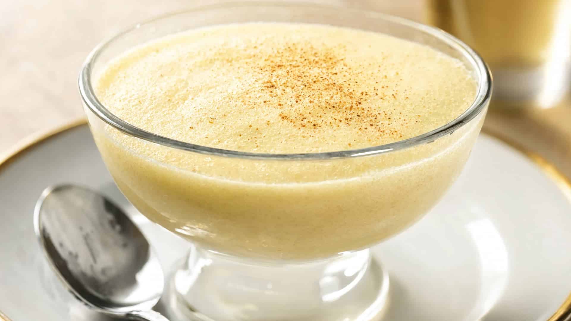 a glass dessert bowl filled with creamy zabaglione custard with a light dusting on top and a spoon resting beside