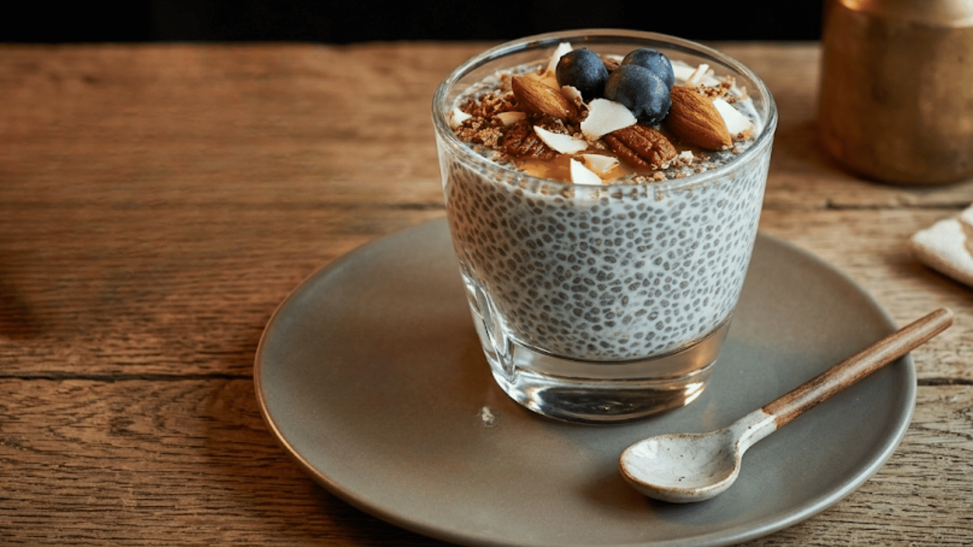 a glass of chia pudding topped with blueberries almonds pecans coconut flakes and honey served as a wholesome breakfast snack