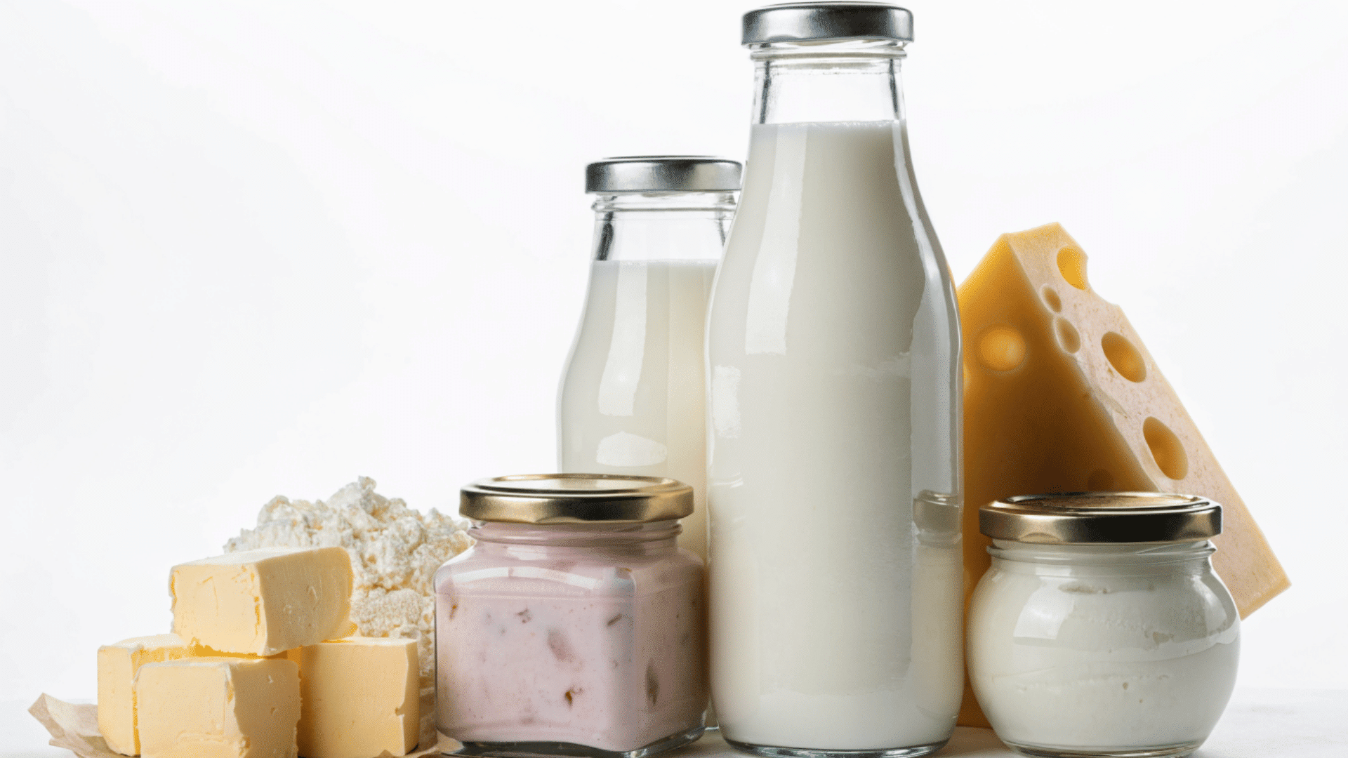 assorted dairy products with milk bottles cheese curd and yogurt jars arranged on a white surface