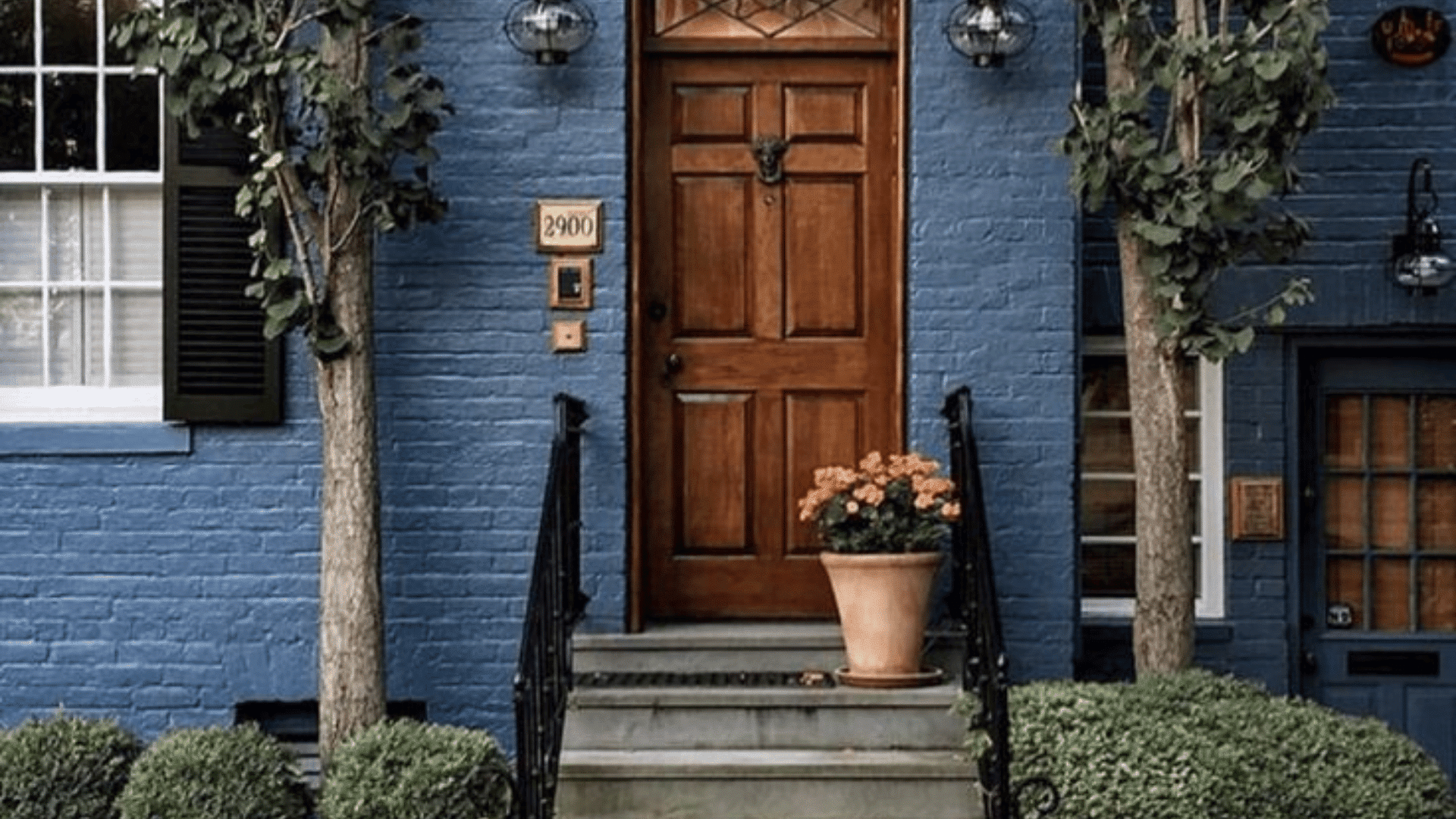 blue brick house with garden beds large windows and a front patio beside the driveway
