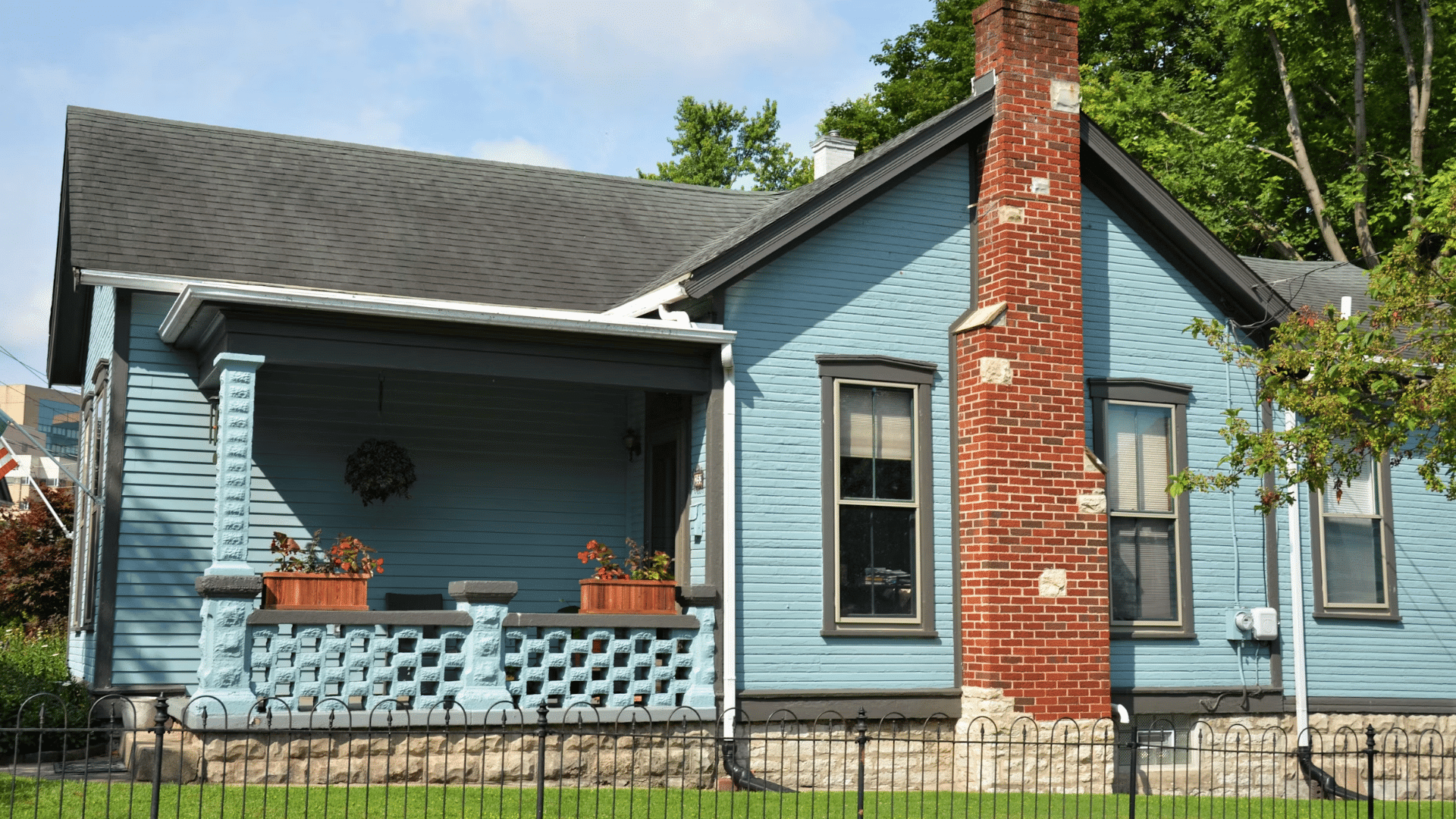 blue wooden house with covered porch red brick chimney and fenced front yard greenery