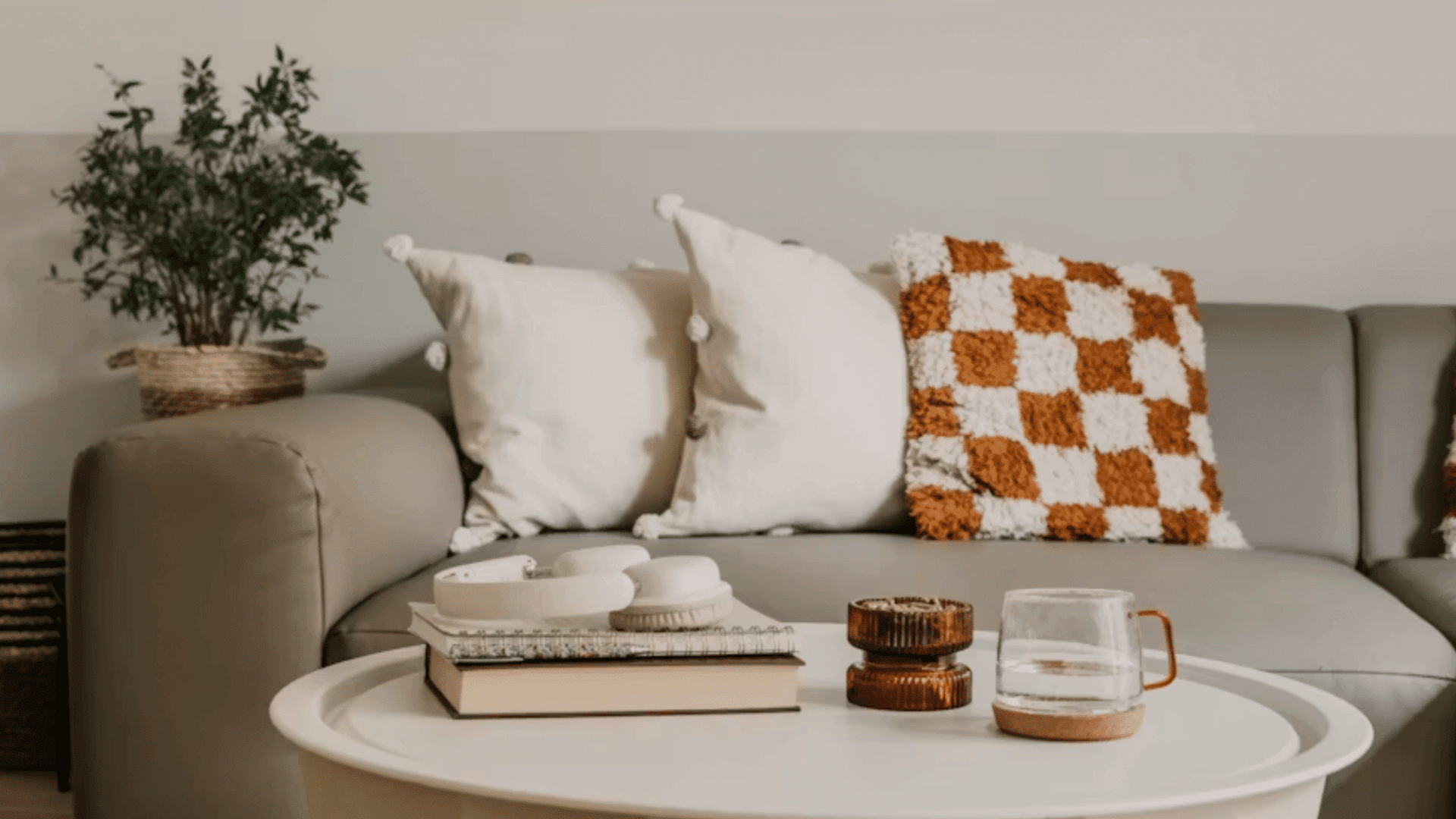books candle and glass mug arranged on a round coffee table in front of a sofa with patterned cushions