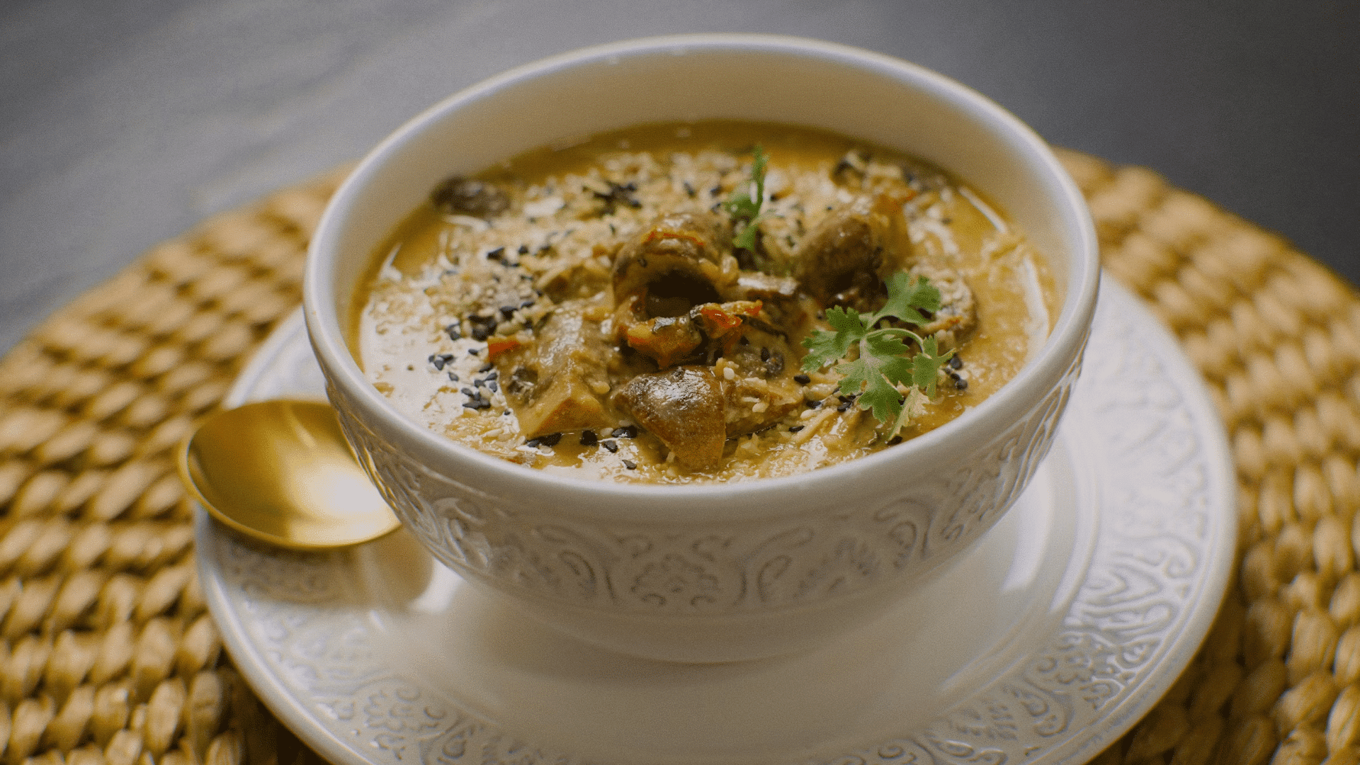 bowl of creamy soup topped with mushrooms herbs and seeds on woven placemat