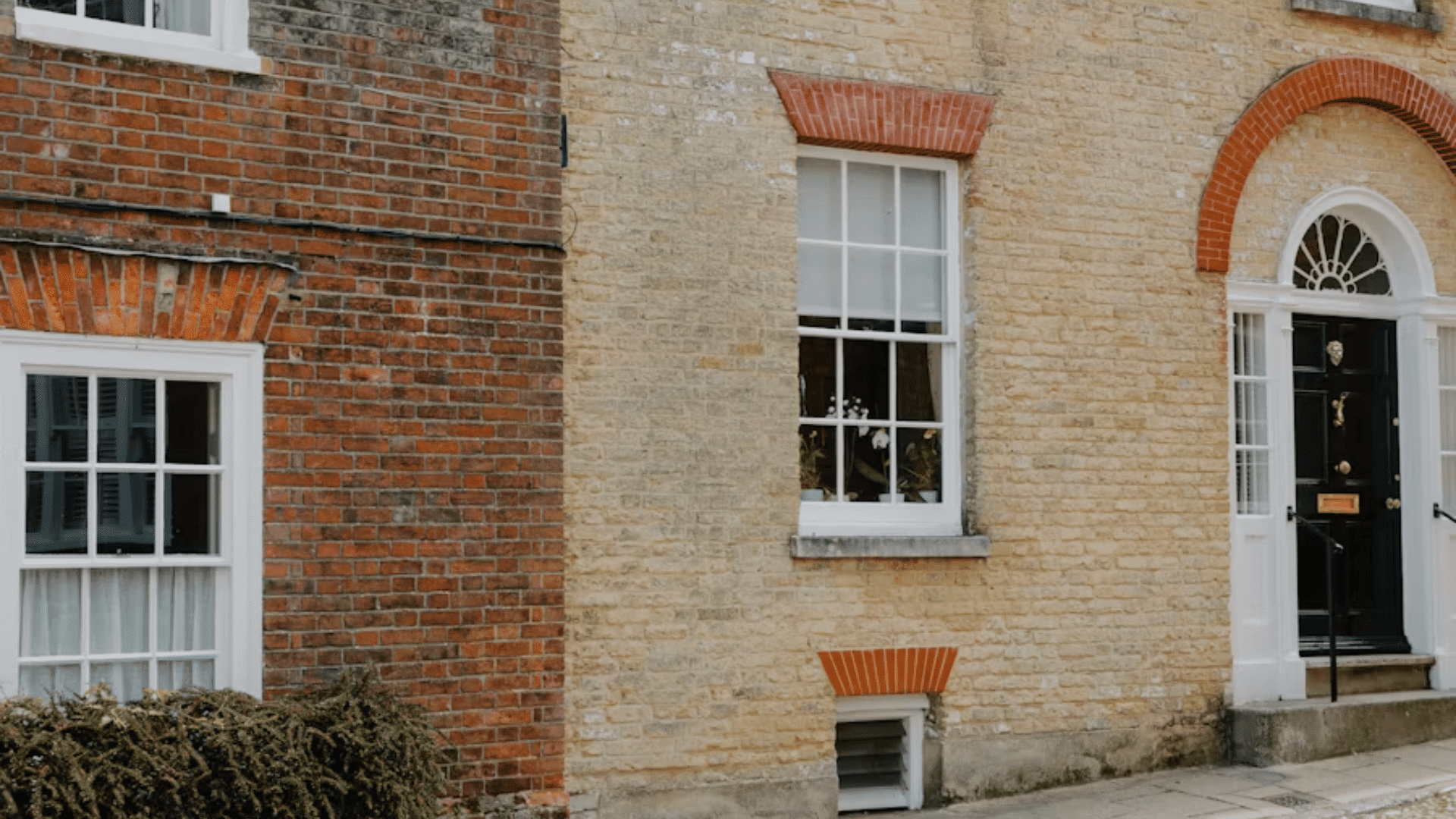 brick and stone house exterior with white windows and black front door beside a paved walkway