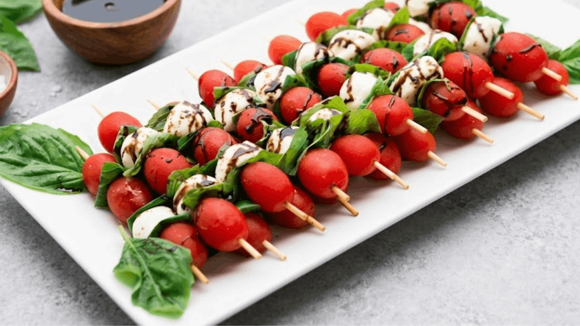 caprese skewers with cherry tomatoes mozzarella balls and fresh basil drizzled with balsamic glaze on a serving platter (1)