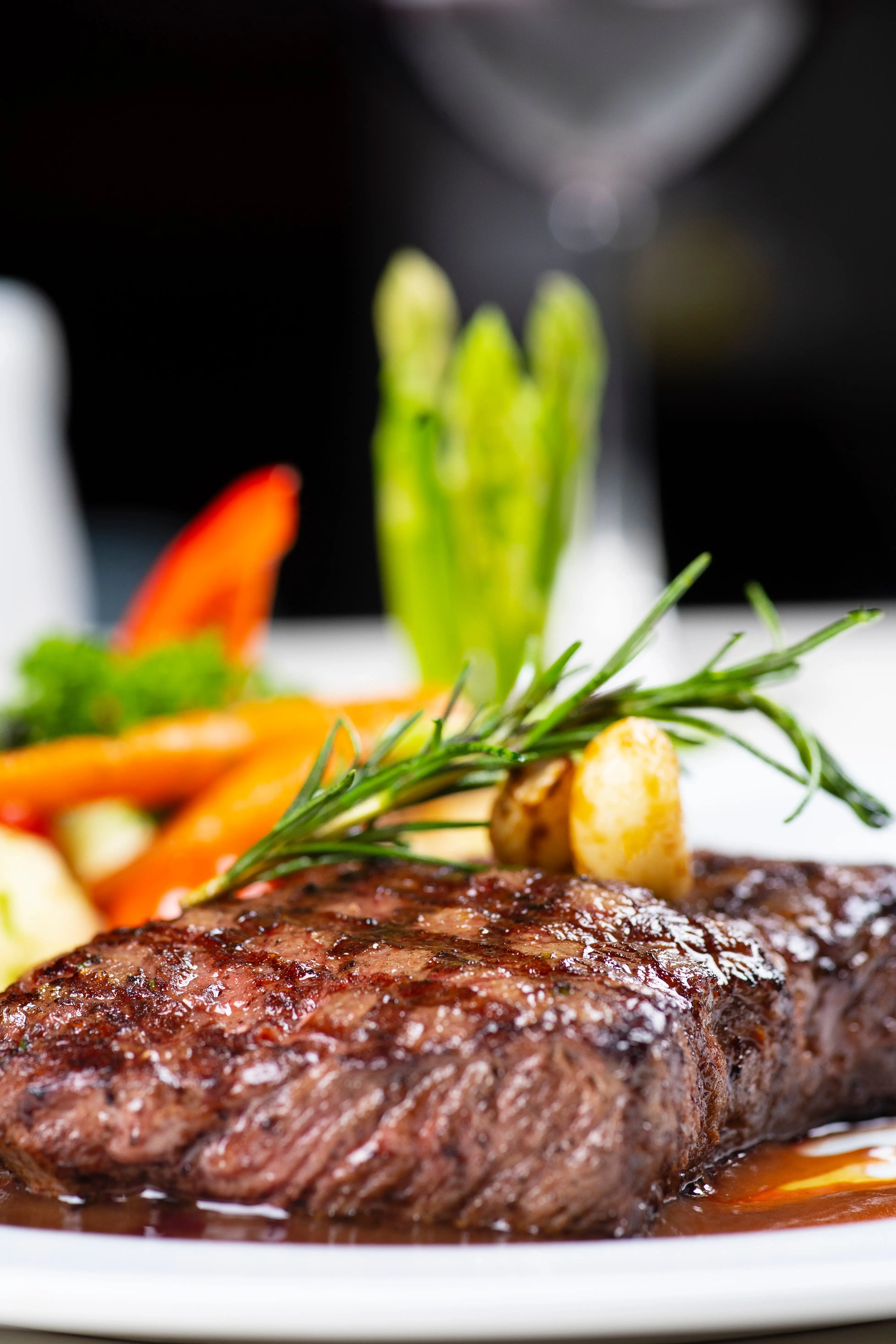 Grilled steak with rosemary garnish and vegetables on a white plate in restaurant setting
