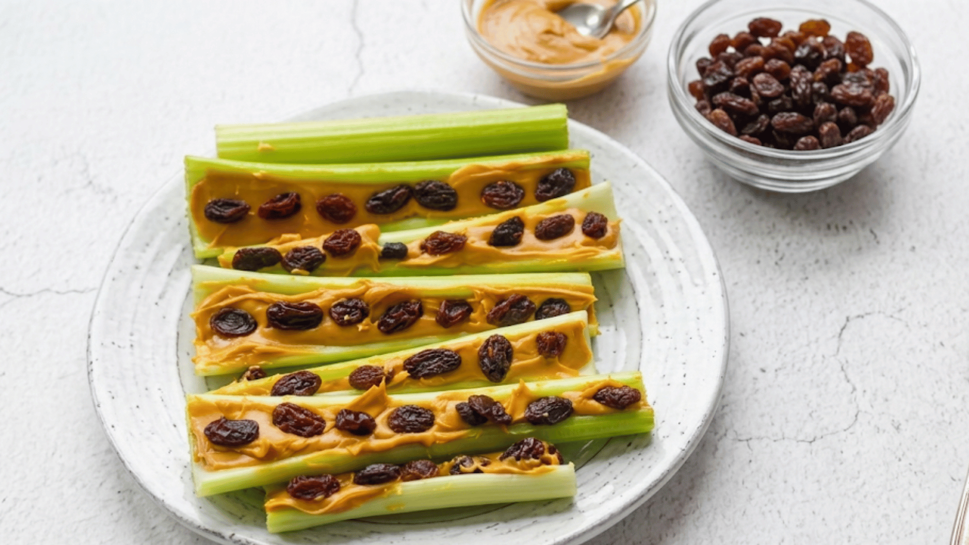 celery sticks filled with peanut butter and topped with raisins on a plate beside small bowls for a simple healthy snack