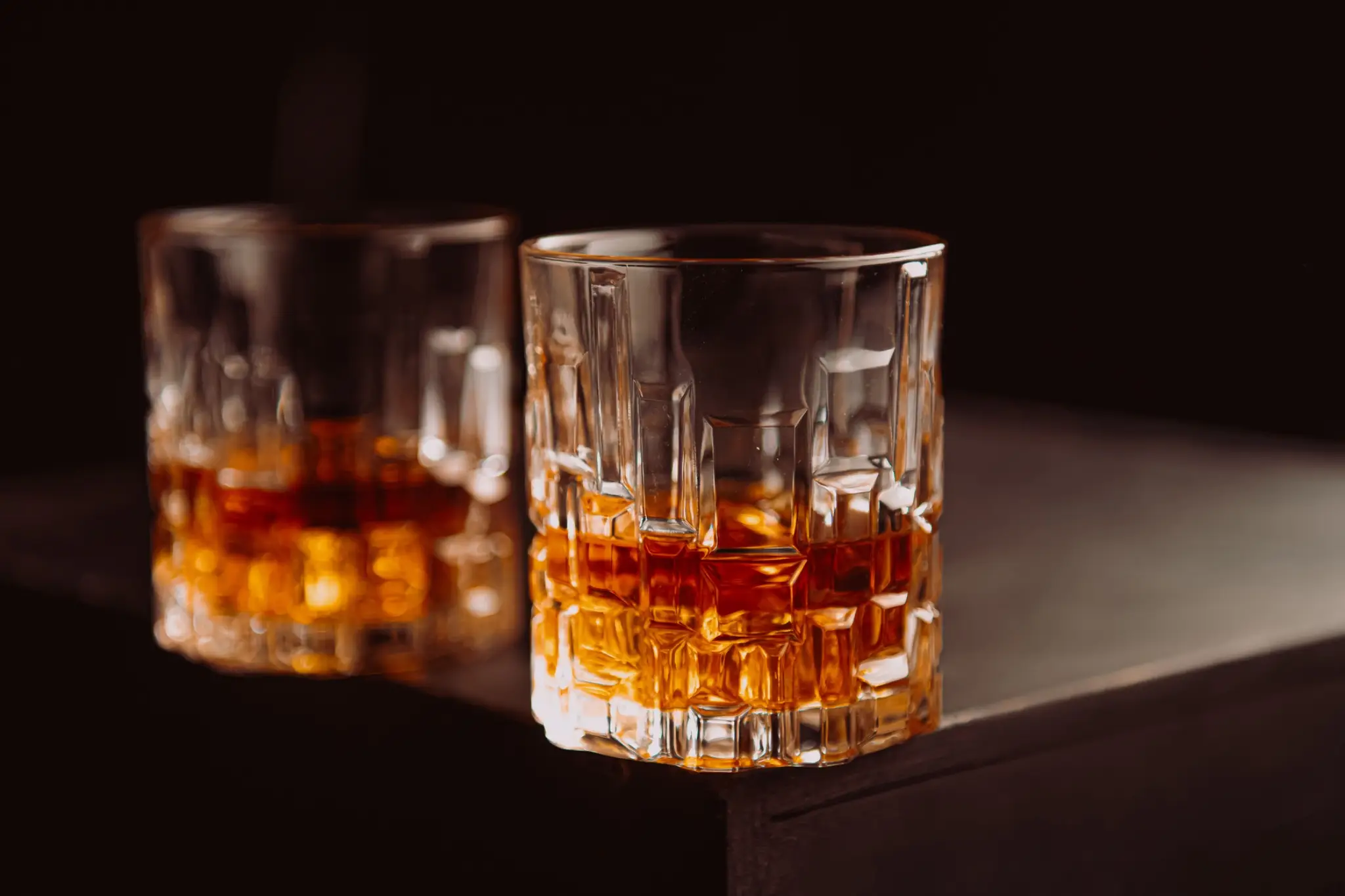 Two crystal glasses filled with amber liquid on dark background with soft lighting