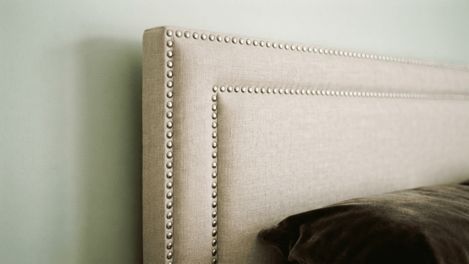 close up of a beige upholstered headboard with decorative nail trim for diy upholstery inspiration