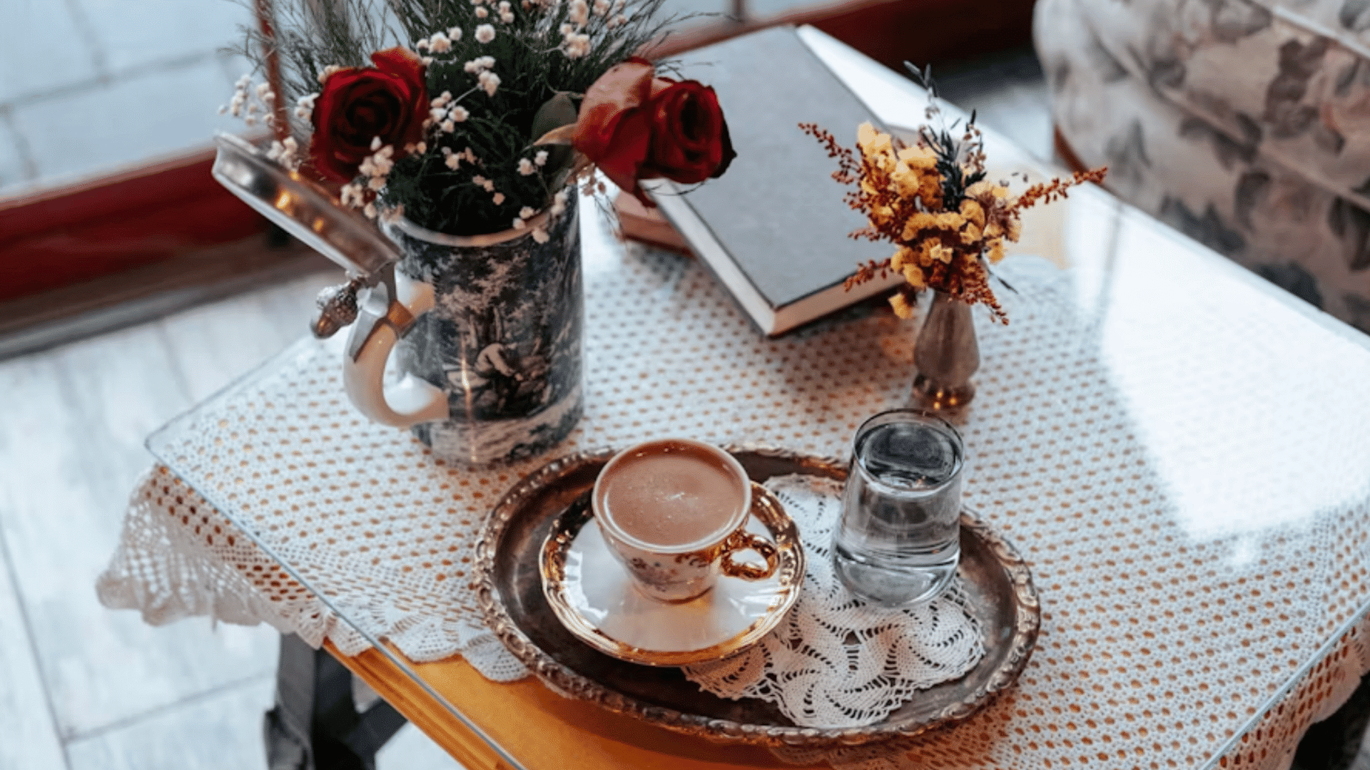 coffee cup with water glass and flower arrangements on a styled coffee table beside decorative books