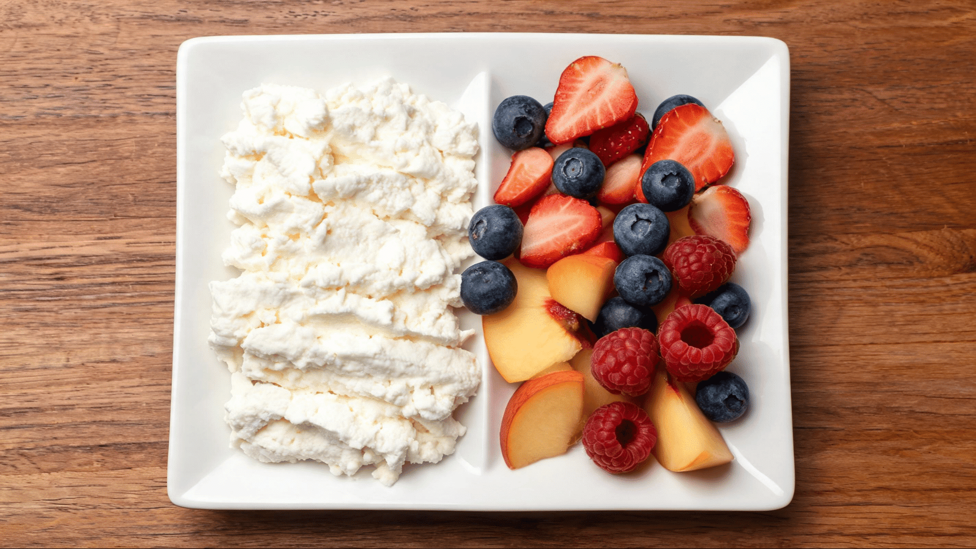 cottage cheese served with strawberries blueberries raspberries and peach slices on a divided white plate