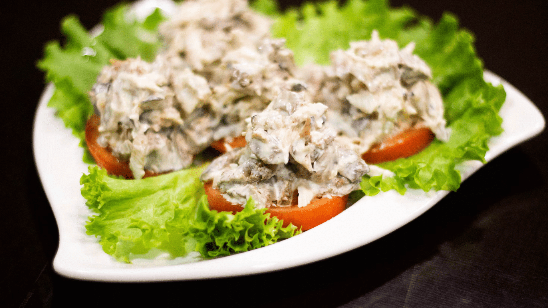 creamy chicken salad served on lettuce leaves with tomato slices on white plate