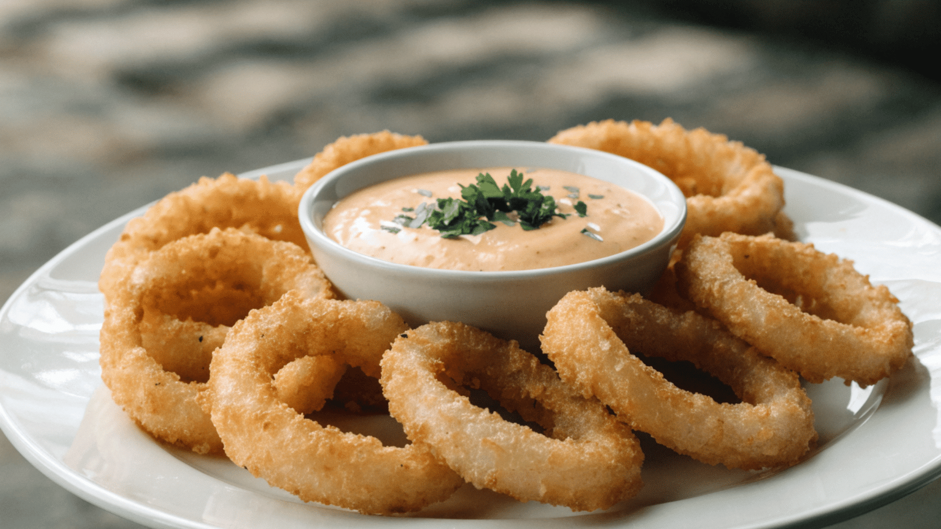 crispy onion rings arranged around a bowl of dipping sauce on a white plate with parsley garnish