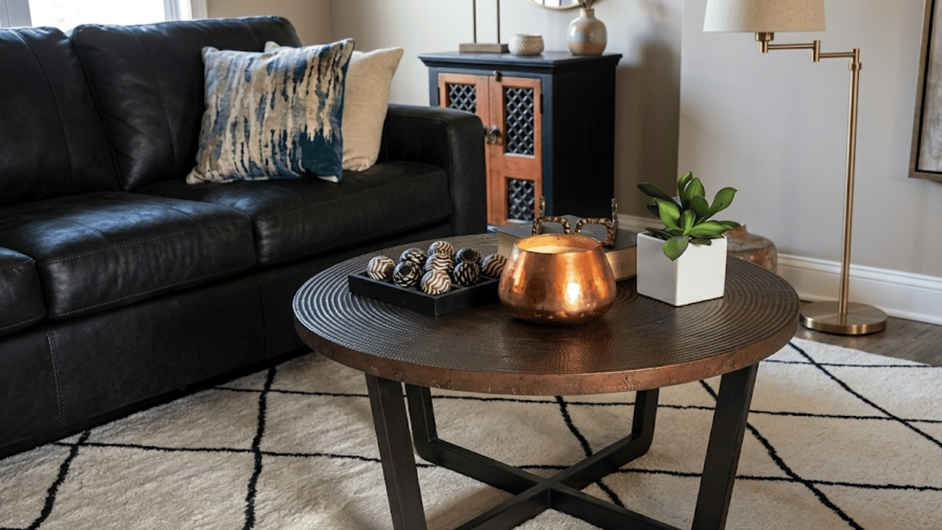 decorative candle books plant and eyeglasses styled neatly on a round coffee table in a cozy living room
