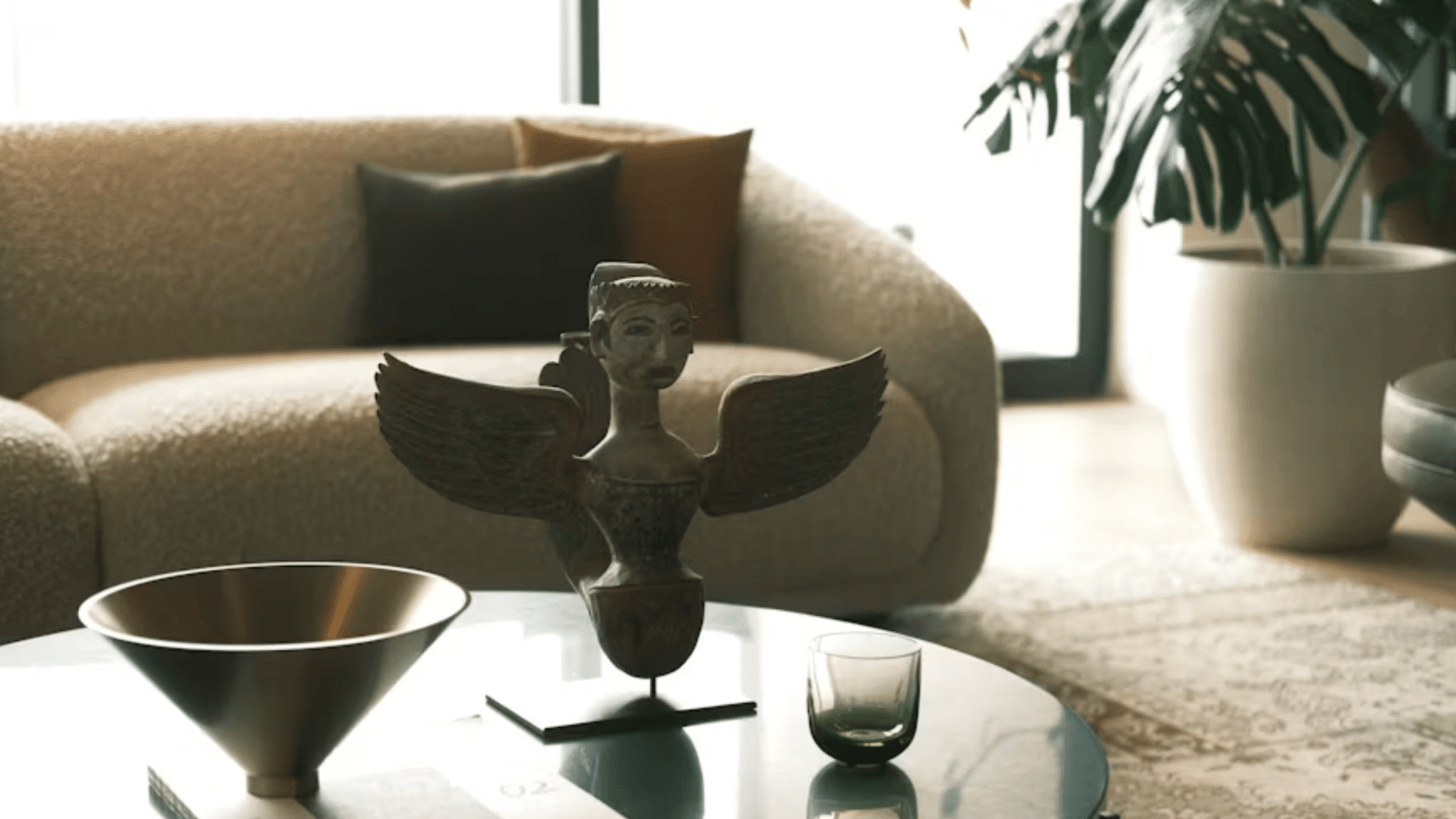decorative winged sculpture with bowl and glass on a round coffee table in a modern living room space