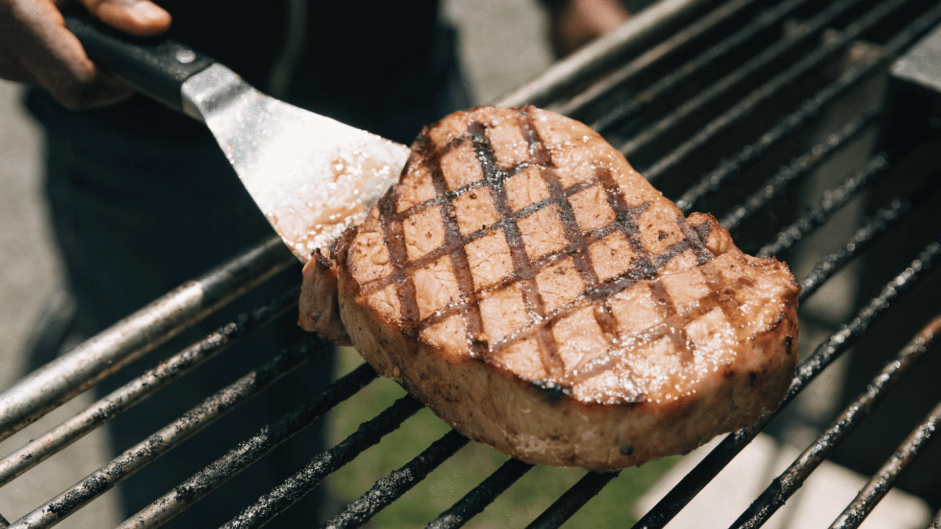 fatty grilled meat steak with crosshatch marks being lifted from a barbecue grill with a spatula