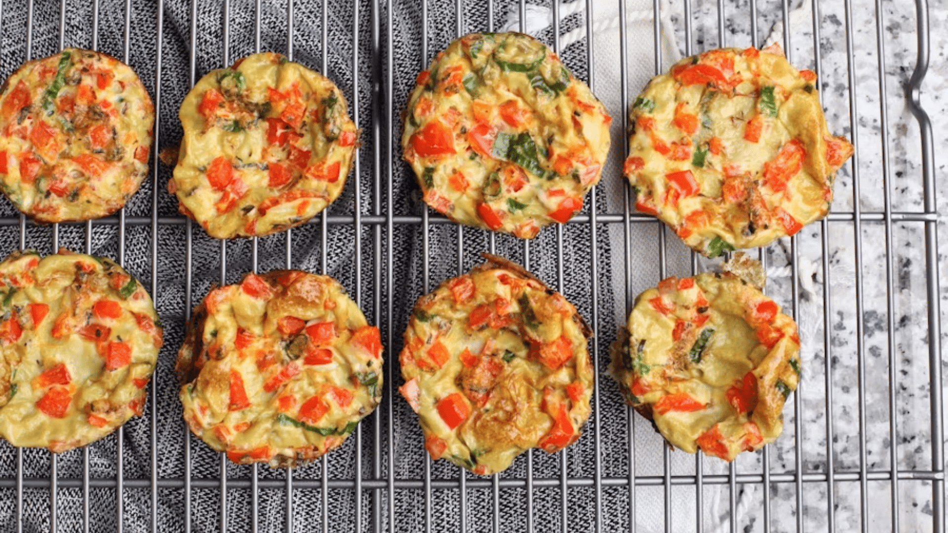 freshly baked egg muffins with red peppers and herbs arranged on a cooling rack