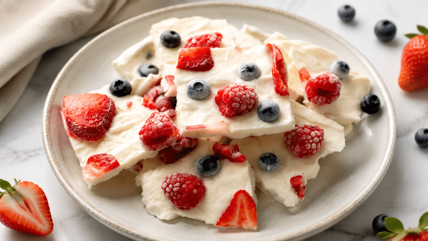 frozen yogurt bark topped with strawberries, raspberries, and blueberries arranged on a ceramic plate with soft natural light