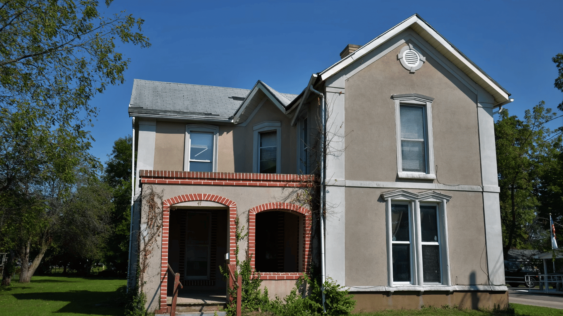 gray stucco house with brick arched porch openings and trees around the front lawn area
