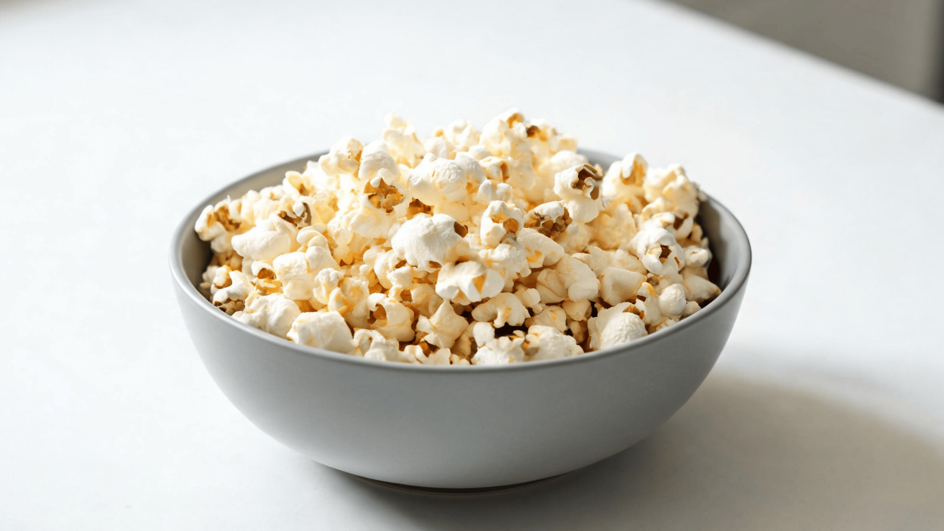 Gray bowl filled with freshly popped popcorn on a bright white table