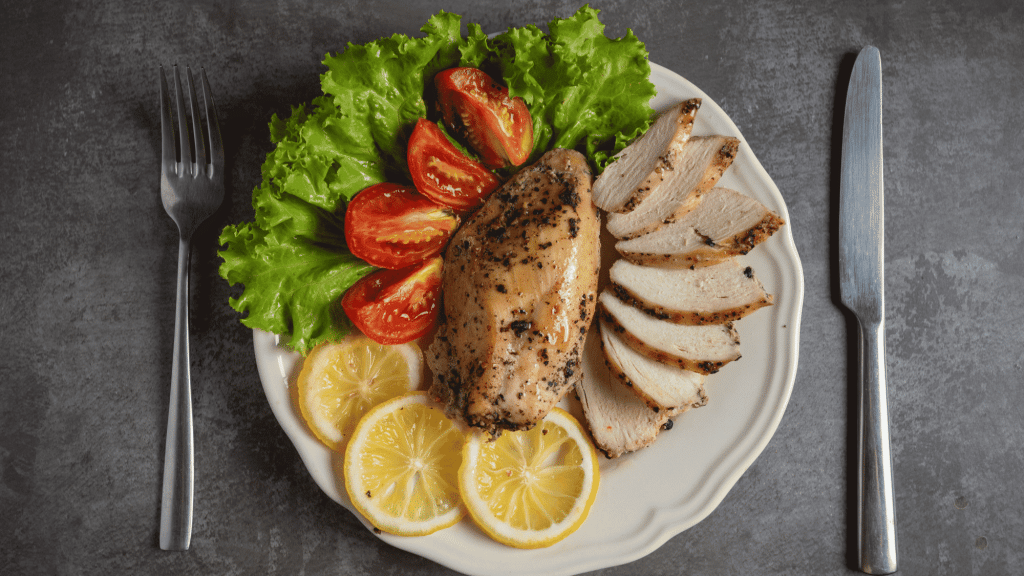 grilled chicken breast served with sliced chicken fresh lettuce tomatoes and lemon on a healthy dinner plate