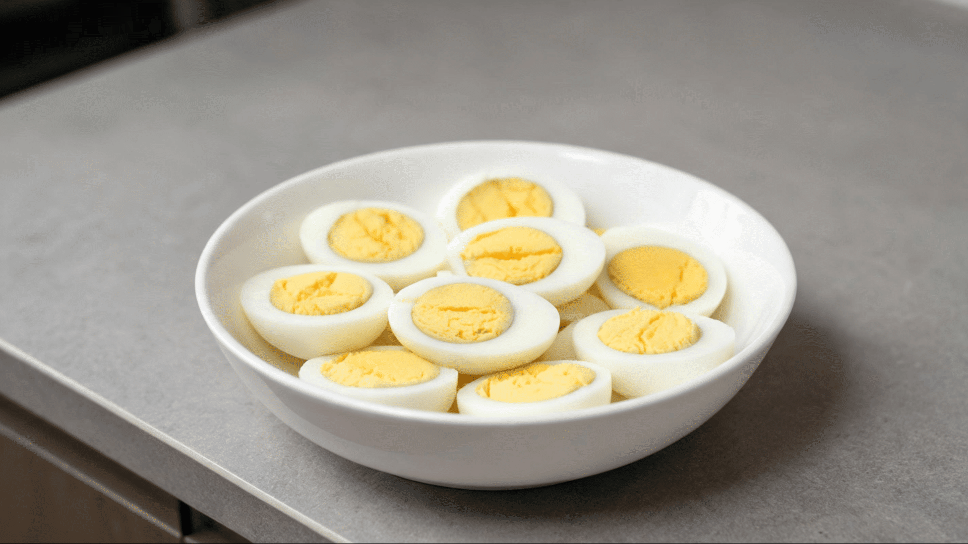 halved hard boiled eggs arranged in a white bowl on a gray kitchen countertop