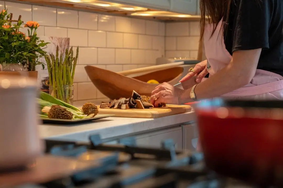 Person chopping mushrooms on wooden board in cozy kitchen with fresh vegetables nearby