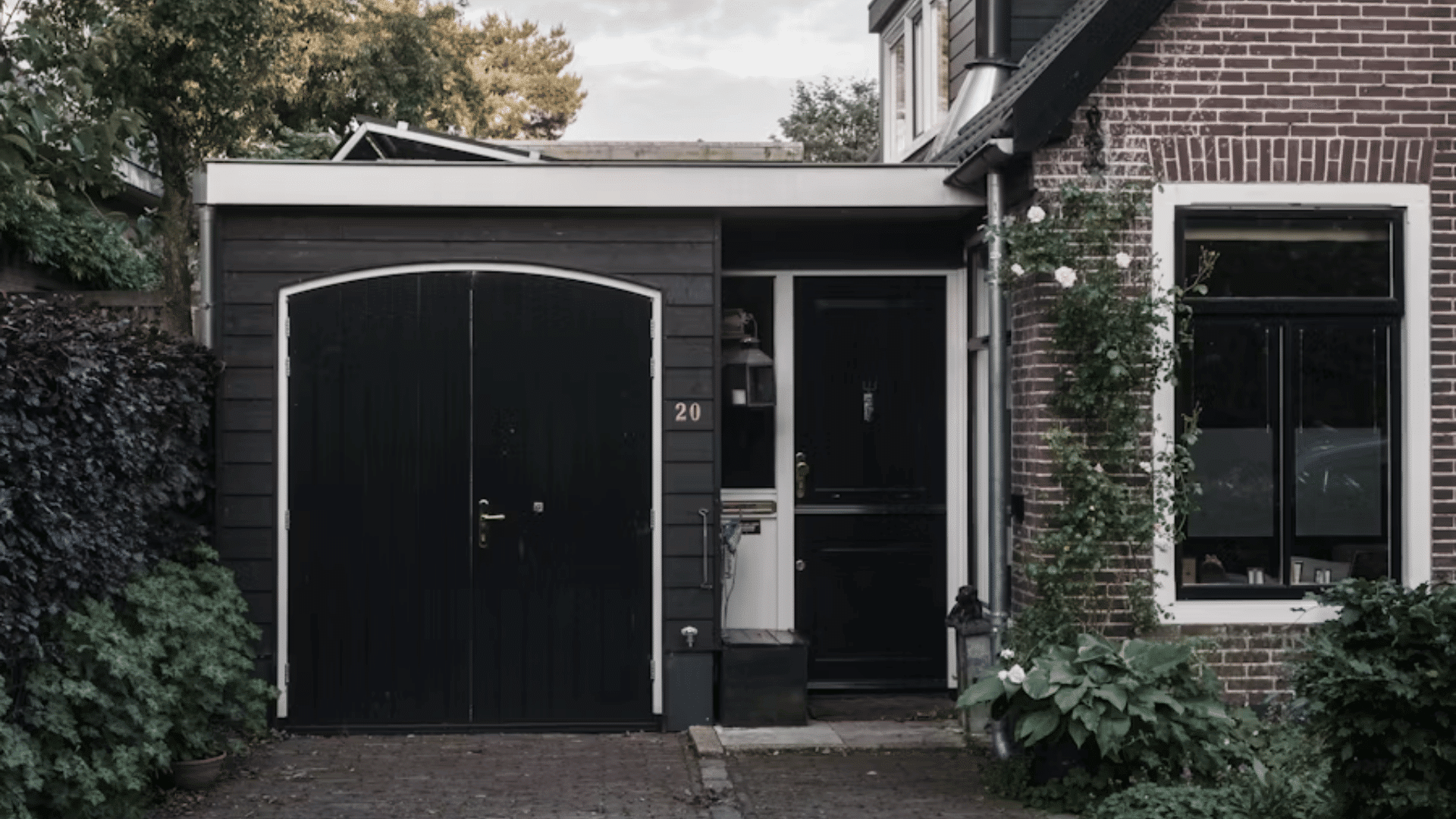 modern brick home with black garage door entrance and plants growing around the driveway