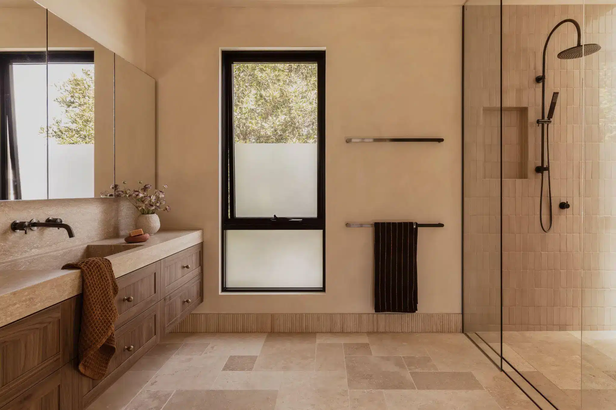 Modern bathroom with wooden vanity, large mirror, glass shower, and neutral tile flooring
