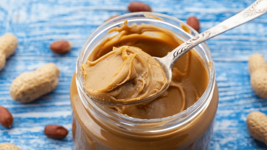 open jar of creamy peanut butter with a spoon peanuts and healthy foods highlighting its nutrition benefits