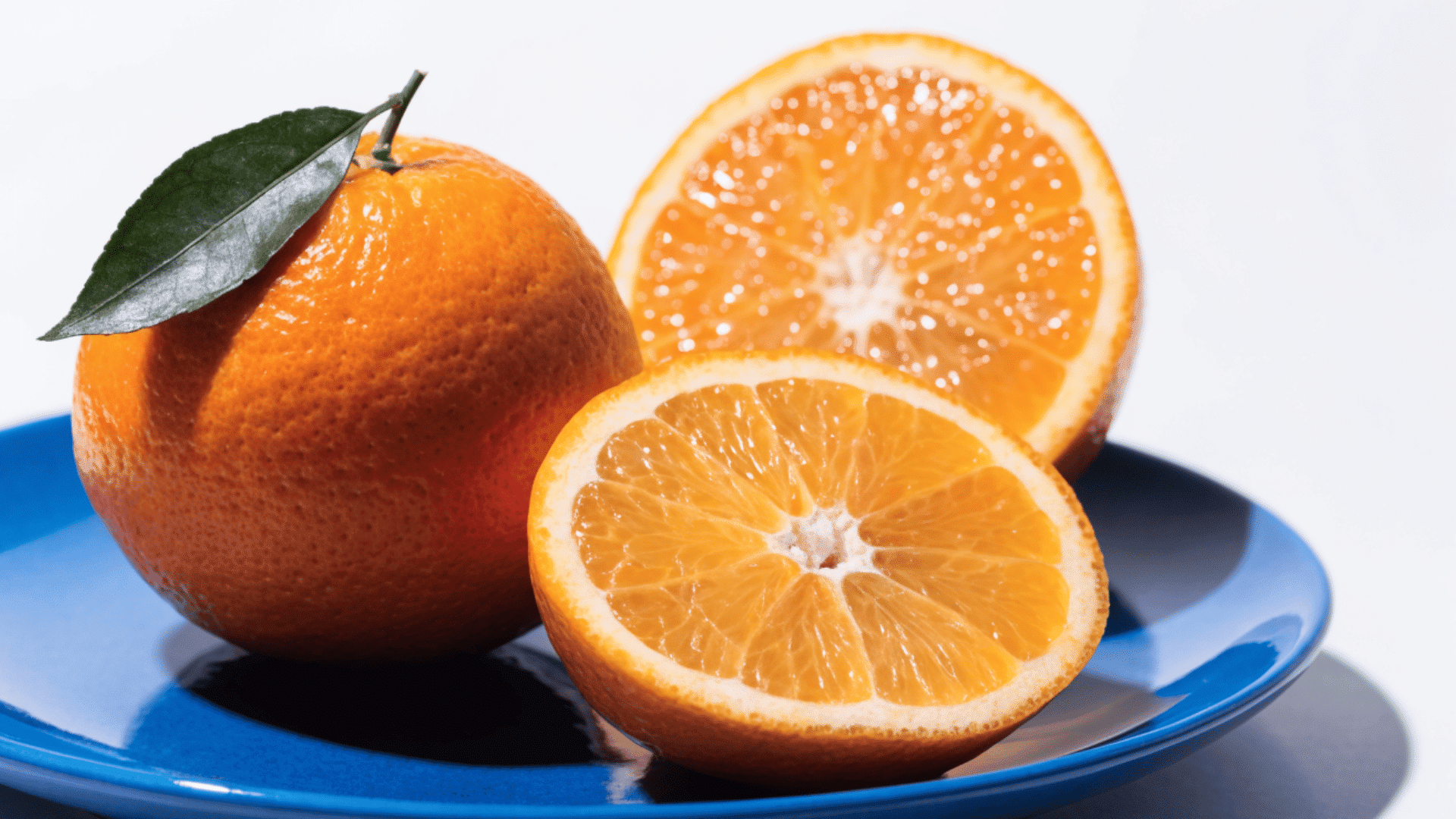 orange citrus fruits with whole and sliced halves placed on a blue plate with a green leaf on white background