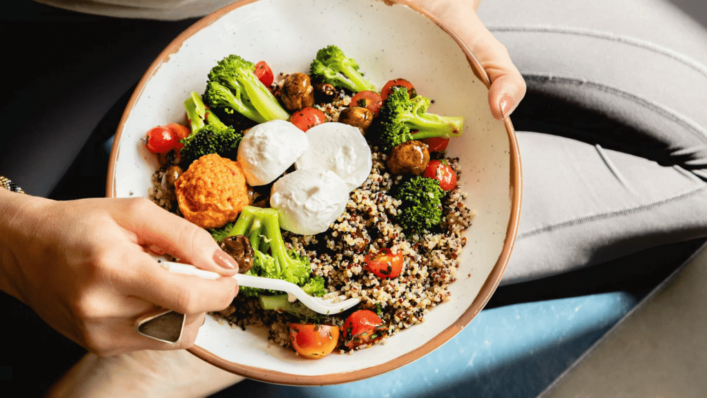 person holding a bowl of quinoa with broccoli tomatoes chickpeas and mozzarella
