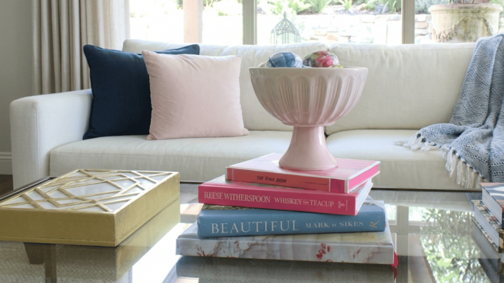 pink decorative bowl on stacked coffee table books with colorful ornaments in a bright living room setting