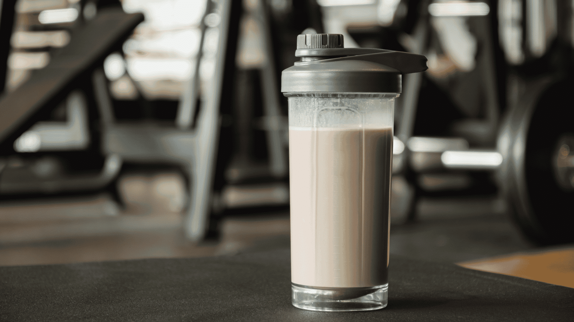 protein shake in a shaker bottle placed on gym floor with workout equipment in background