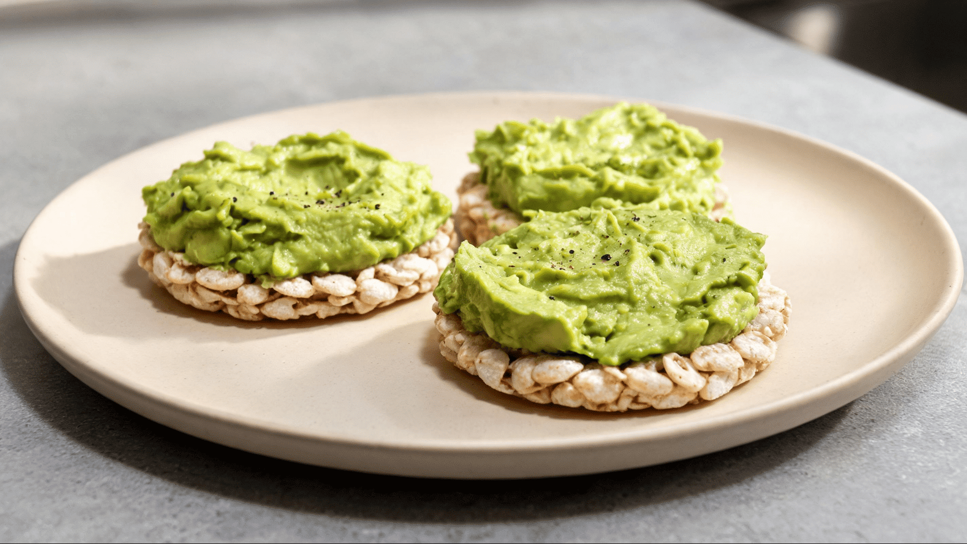 Rice cakes topped with mashed avocado and black pepper served on a beige plate