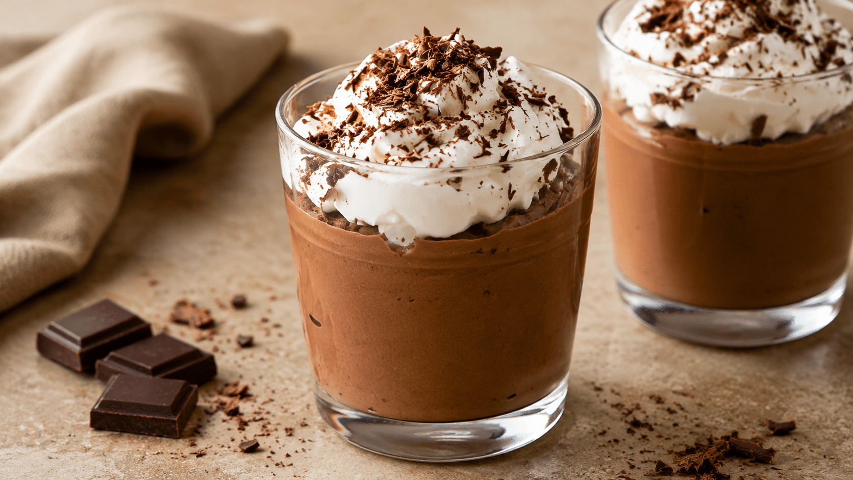 rich chocolate mousse topped with whipped cream and dark chocolate shavings served in glass dessert cups on a rustic tabletop