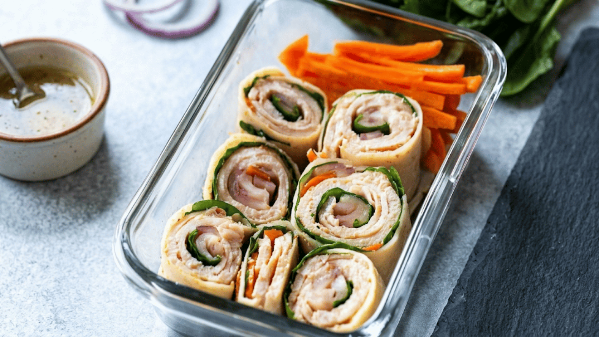 sliced turkey roll ups with spinach and carrots in a glass container served with dipping sauce for a healthy meal prep lunch (1)