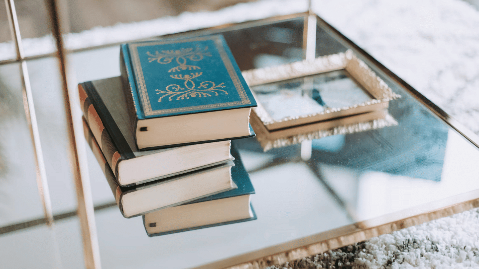 stack of hardcover books beside a small decorative tray on a glass coffee table over a soft textured rug