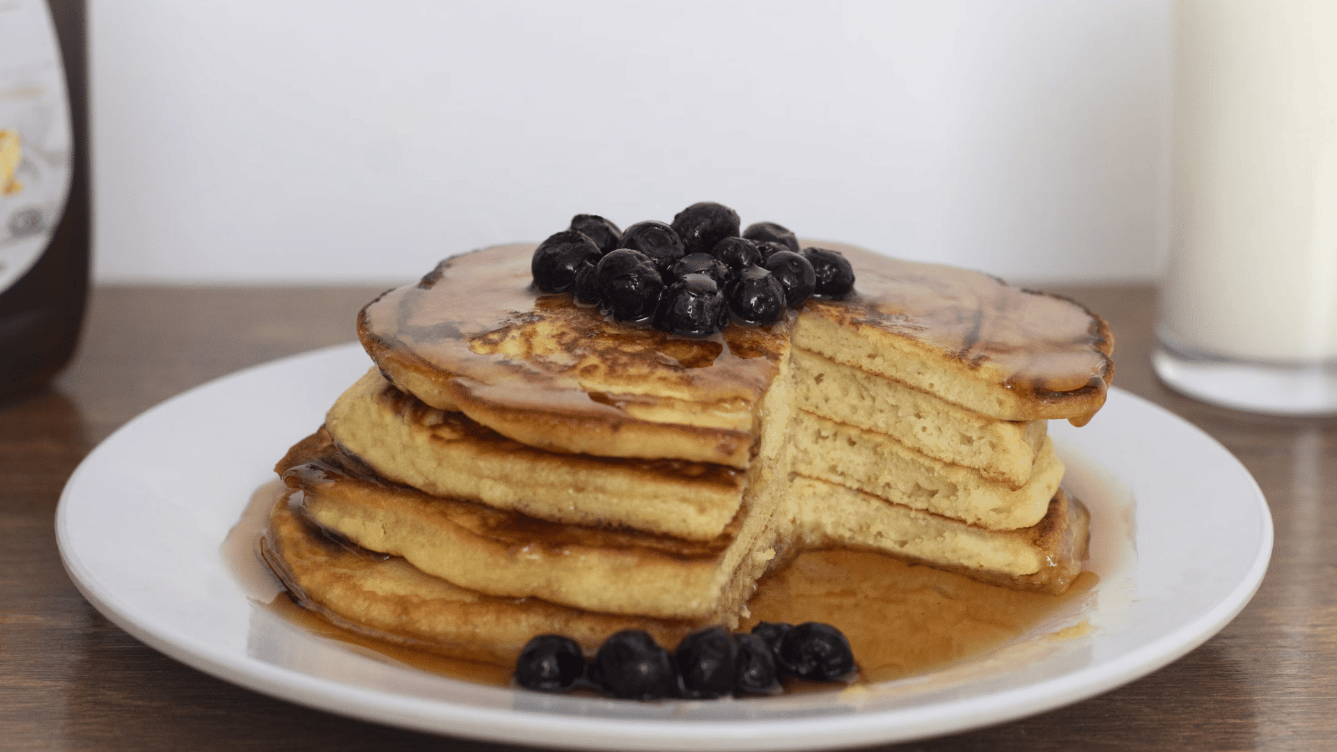 stack of pancakes topped with blueberries and syrup on a white plate