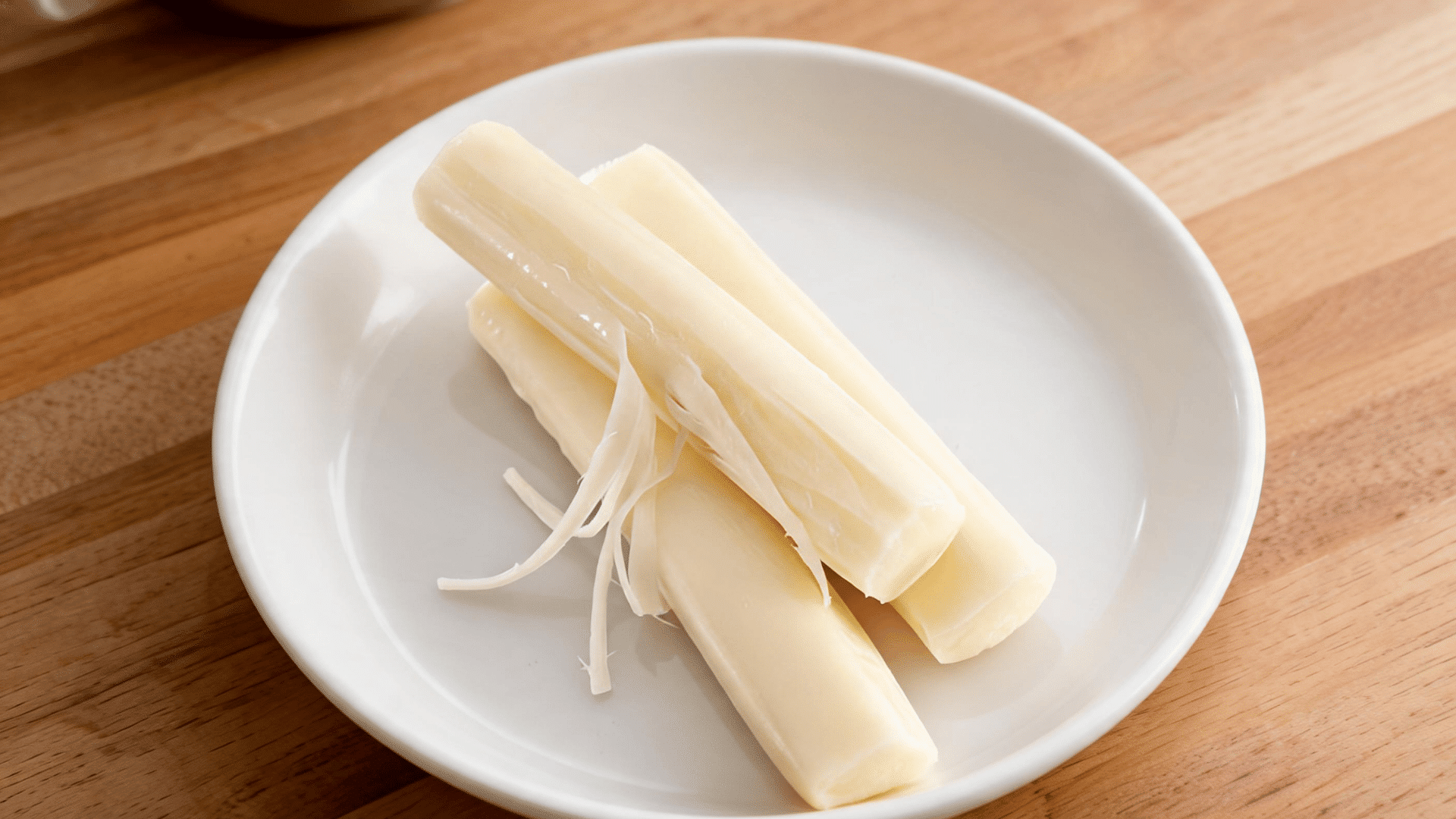 string cheese sticks arranged on a white plate over a wooden table